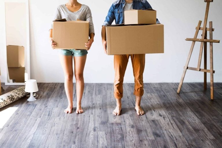 A couple holding moving boxes in a clean and organized home.